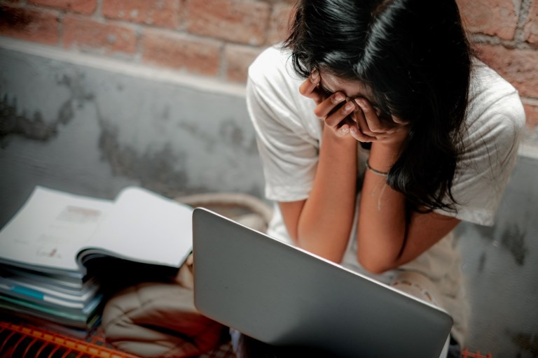 Asian teen girl in casual white shirt cover her face with both hands in front of a laptop. Feeling tired and depressed of studying